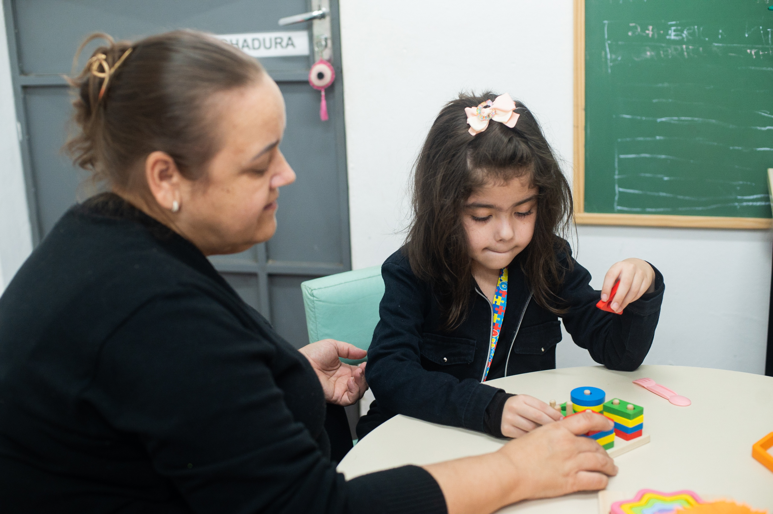 Professora auxiliando aluna com material pedagógico